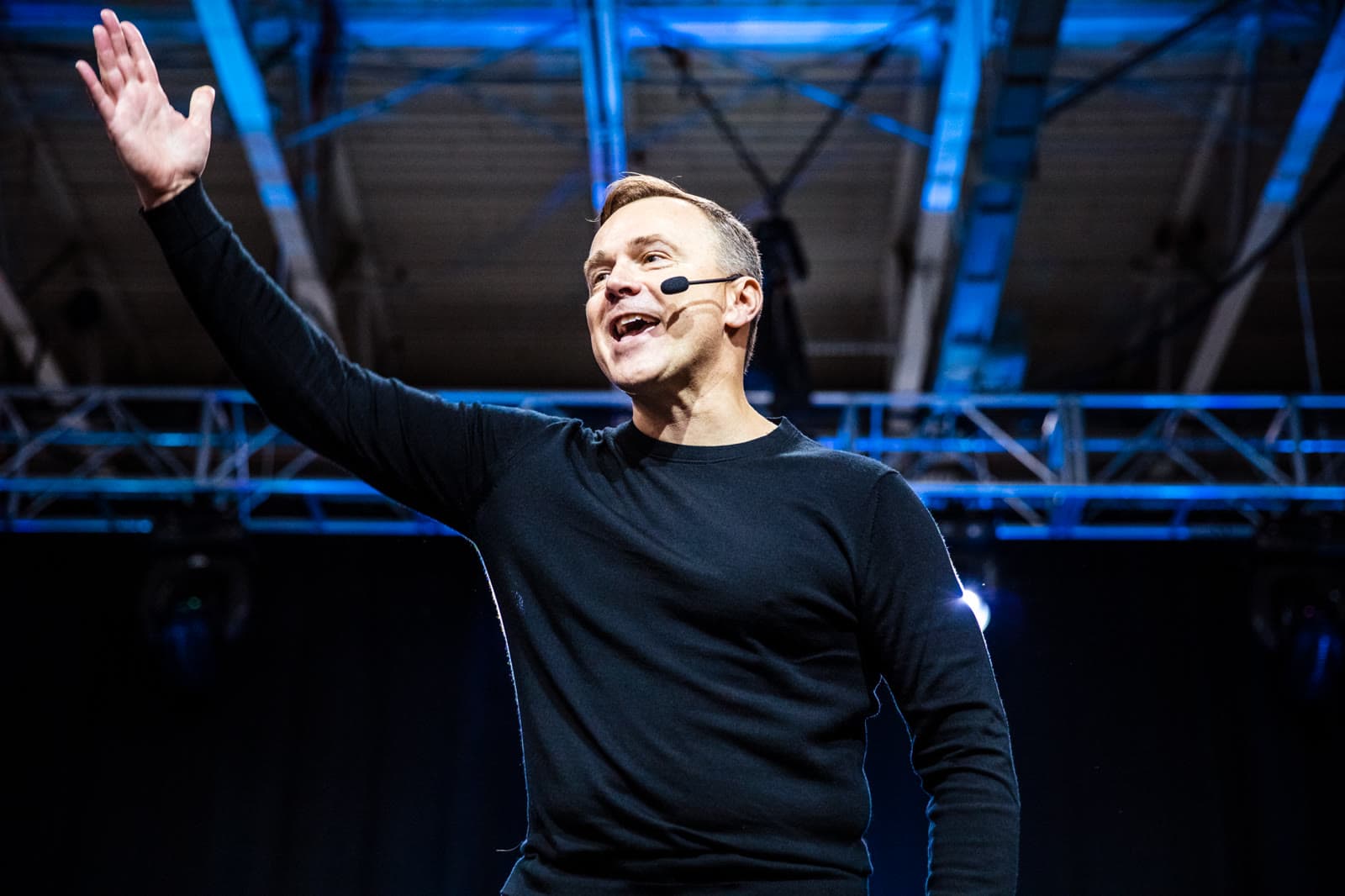 Sean Callagy on stage at a live event, arm raised, greeting the room